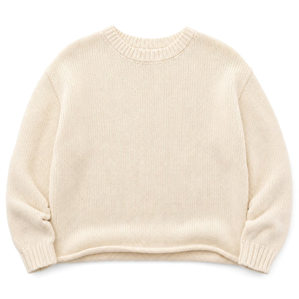 Frau trägt cremeweißen Baumwoll-Strickpullover mit rundem Kragen und Handgelenklänge