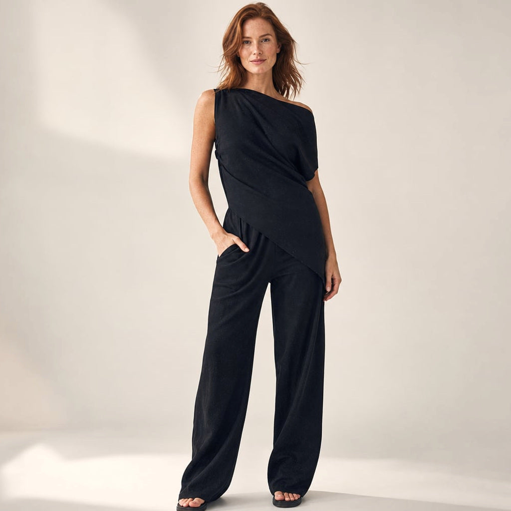 Model trägt schwarzes Off-Shoulder-Set mit diagonalem Ausschnitt und weit fallender Hose
