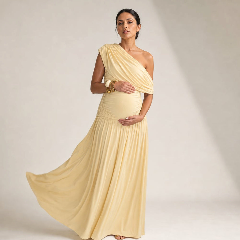 Schwangere Frau trägt apricotfarbenes One-Shoulder Maxi-Kleid mit weitem Fall bis zum Boden